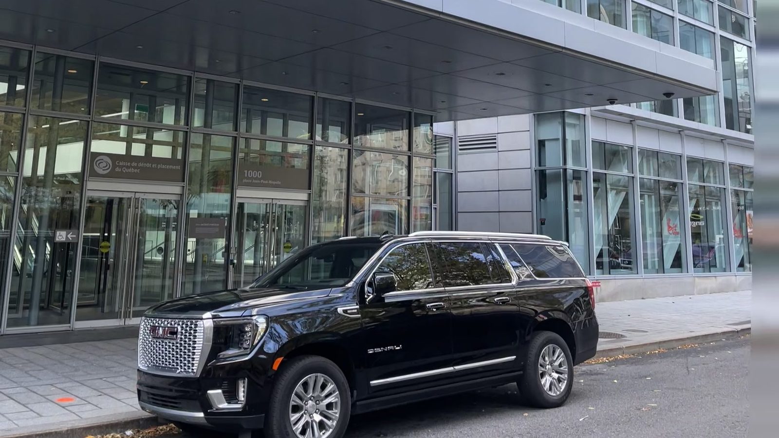 VUS GMC Denali noir devant l'entrée d'une tour de bureaux au centre-ville de Montréal