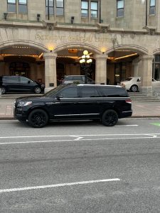 A luxurious Navigator Limousine from MtlPrimeLimos parked alongside the front entrance of Fairmont Château Royal in Ottawa, viewed from across the entrance.